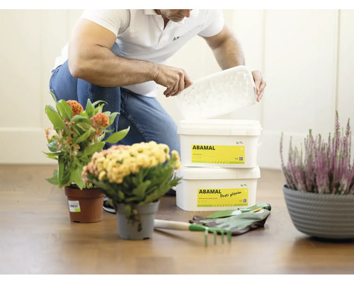 Osoba otevírá nádobu s přípravkem na ochranu rostlin vedle rostlin a zahradního nářadí.