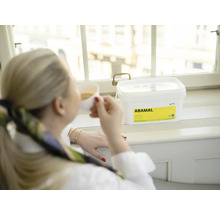 Žena pije kávu vedle kbelíku fasádní barvy Abamal na okenním parapetu.