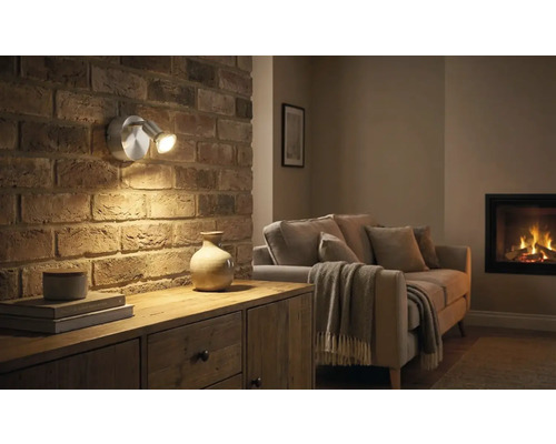 Obývací pokoj s cihlovou zdí, komodou a dvouramenným nástěnným svítidlem