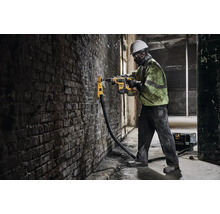 Stavební dělník vrtá vrtačkou otvor do cihlové zdi.