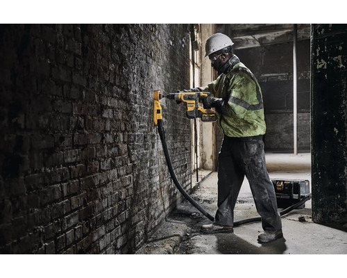 Stavební dělník vrtá vrtačkou otvor do cihlové zdi.