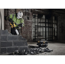 Pracovník opracovává zeď pomocí vrtacího kladiva a odsávání prachu.