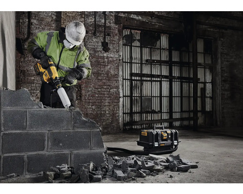 Pracovník opracovává zeď pomocí vrtacího kladiva a odsávání prachu.