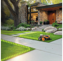 Robotická sekačka seká trávník před moderním domem s kamennou fasádou a velkou zahradou.