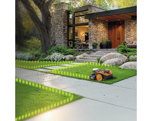 Robotická sekačka seká trávník před moderním domem s kamennou fasádou a velkou zahradou.