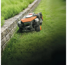 Robotická sekačka LandRoid na trávníku vedle kamenné zdi