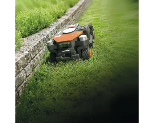 Robotická sekačka LandRoid na trávníku vedle kamenné zdi
