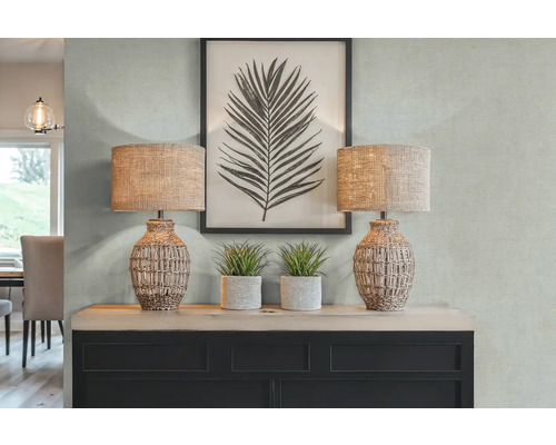 Dekorativní interiér se dvěma stolními lampami, umělými rostlinami a zarámovaným potiskem listů na komodě.