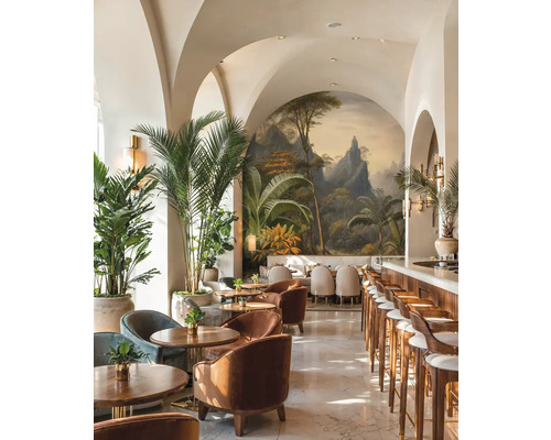 Světlý bar s klenutými stropy, tropickou nástěnnou malbou, dřevěným nábytkem, sametovými křesly a velkými palmami v květináčích.