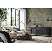 Moderní obývací pokoj se světlou pohovkou, koženým taburetem a vliesovou fototapetou s motivem palem na stěně za komodou.