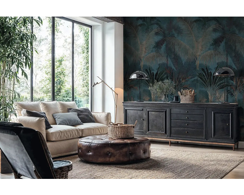 Obývací pokoj s fototapetou s motivem palem v tmavě modré a zlaté barvě, světlou pohovkou, koženým taburetem a černou komodou u velkých oken.