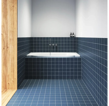 Moderní koupelna s modrými čtvercovými obklady na stěně a podlaze, bílou vanou a nástěnnou chromovou baterií.