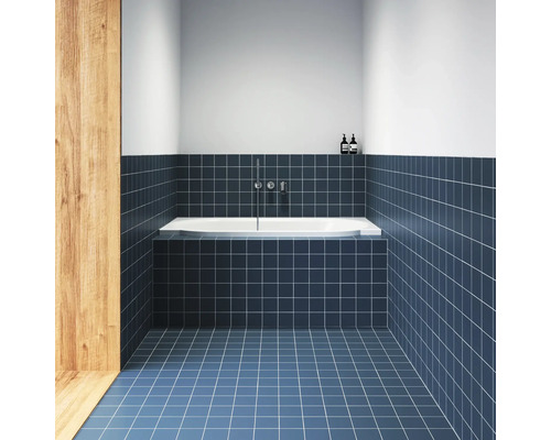 Moderní koupelna s modrými čtvercovými obklady na stěně a podlaze, bílou vanou a nástěnnou chromovou baterií.