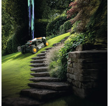 Scéna s robotickou sekačkou na trávu na zeleném trávníku vedle kamenného schodiště