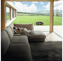 Chlapec spí na gauči, zatímco robotická sekačka pracuje na zahradě