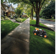 Robotická sekačka seká trávník před obytným domem.