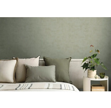 Moderní ložnice s polštáři v zelené a krémové barvě před strukturovanou olivově zelenou stěnou a rostlinou toulitka.