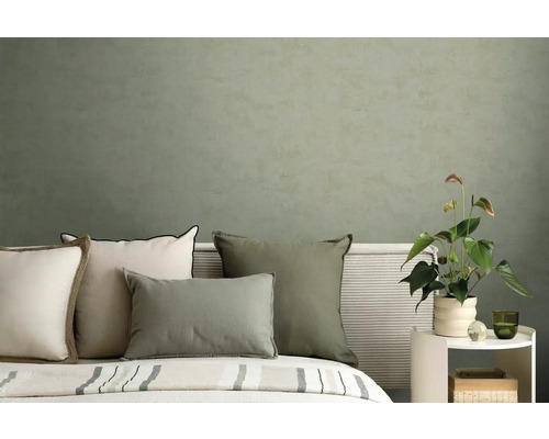 Moderní ložnice s polštáři v zelené a krémové barvě před strukturovanou olivově zelenou stěnou a rostlinou toulitka.