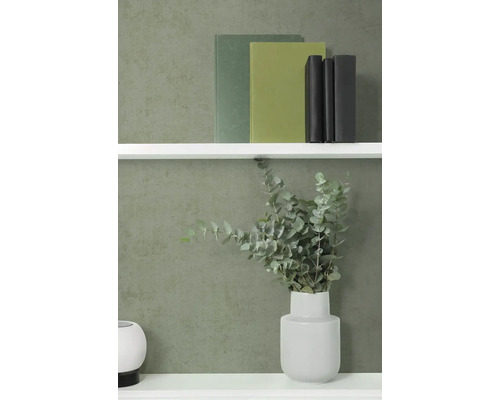 Vliesová tapeta s jemnou strukturou v tmavě zelené barvě na stěně za bílou policí s knihami a vázou s eukalyptem.