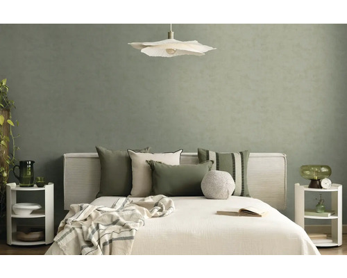 Moderní ložnice s texturovanou šalvějově zelenou tapetou, bílou postelí s polštáři, závěsným svítidlem ve tvaru květu a nočními stolky.