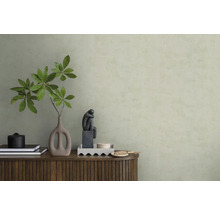 Strukturovaná světle zelená tapeta za dřevěnou komodou s vázou, větvemi a plastikou v minimalistickém interiéru.