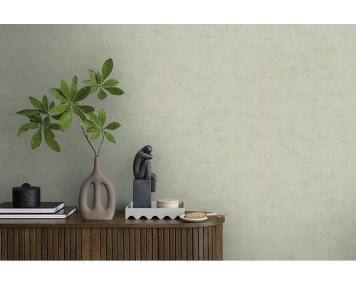 Strukturovaná světle zelená tapeta za dřevěnou komodou s vázou, větvemi a plastikou v minimalistickém interiéru.