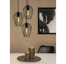 Tři černá závěsná svítidla s drátěnými stínidly nad jídelním stolem s dekorací