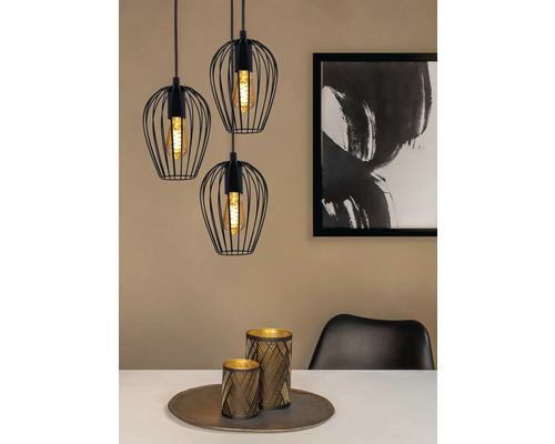 Tři černá závěsná svítidla s drátěnými stínidly nad jídelním stolem s dekorací