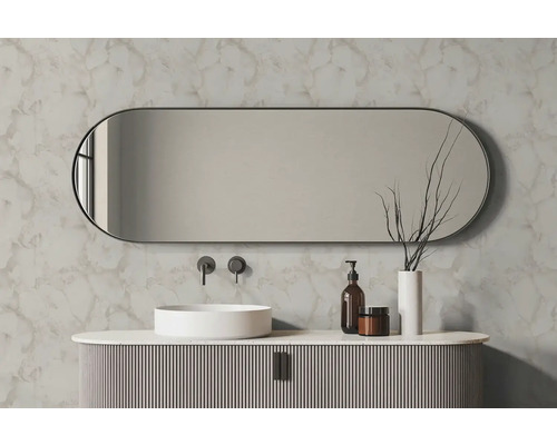 Oválné koupelnové zrcadlo nad bílým umyvadlem na desku a drážkovanou skříňkou před stěnou s mramorovým dekorem.