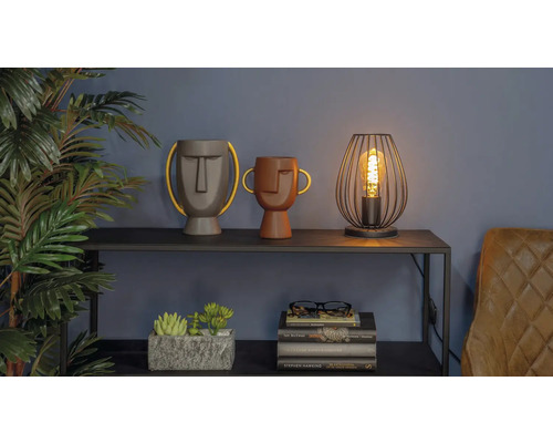 Dekorativní scéna se dvěma vázami s obličeji, lampou a hromadou knih na polici.