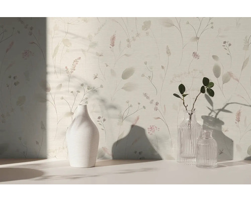Světlá tapeta s jemným květinovým vzorem a trávami, před kterou stojí bílá keramická váza a dvě skleněné vázy na světlém povrchu.