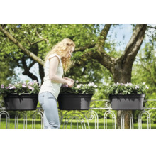 Žena se stará o květiny v truhlících na zábradlí balkonu