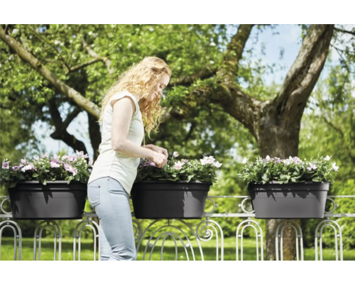 Žena se stará o květiny v truhlících na zábradlí balkonu