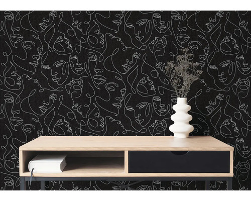 Moderní interiér s tapetou s bílými obličeji v designu one-line art na černém pozadí. Před ní stojí dřevěný příborník s vázou.