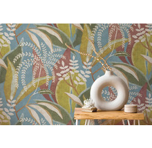 Vliesová tapeta s velkým vzorem listů v modré, zelené a hnědé barvě za dřevěným stolkem s kulatou bílou vázou.