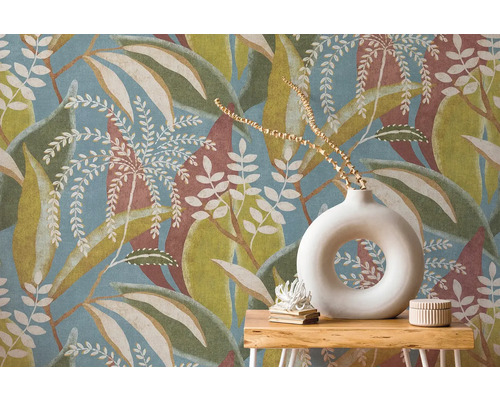 Vliesová tapeta s velkým vzorem listů v modré, zelené a hnědé barvě za dřevěným stolkem s kulatou bílou vázou.