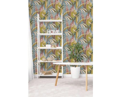 Vliesová tapeta s botanickým vzorem listů v zelené a hnědé barvě na modrém pozadí, bílá police a dřevěný stůl ve světlém pokoji.
