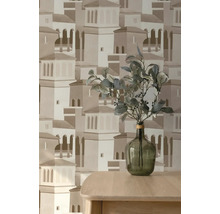 Vliesová tapeta s architektonickým vzorem středomořského města, před ní dřevěný stůl se skleněnou vázou a zelenými větvemi.