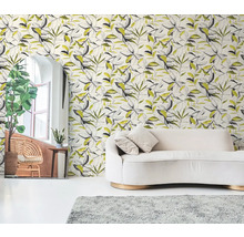 Vliesová tapeta s botanickým vzorem listů v černé a žluté barvě za krémovou pohovkou ve světlém obývacím pokoji.