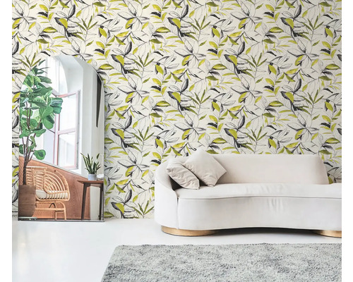 Vliesová tapeta s botanickým vzorem listů v černé a žluté barvě za krémovou pohovkou ve světlém obývacím pokoji.