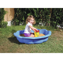 Dívka si hraje na zahradě v modrém pískovišti s hračkami do písku.