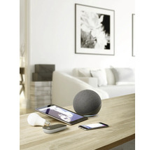 Snímek obývacího pokoje s chytrými domácími zařízeními, jako jsou reproduktory, tablety, smartphony a žárovky na stole.