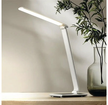 Bílá LED stolní lampa na stole, vedle vázy s rostlinami