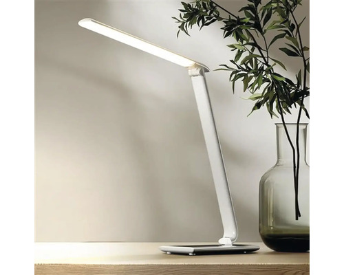 Bílá LED stolní lampa na stole, vedle vázy s rostlinami