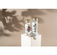 Dvě hřbitovní svíčky s květinovými motivy na bílém podstavci.