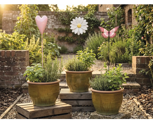 Tři květináče s bylinkami a ozdobné zahradní zápichy ve tvaru srdce, květiny a motýla v zahradě.