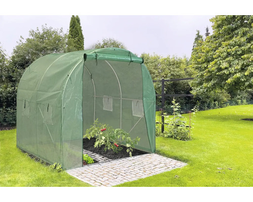 Zelený fóliový skleník s otevřenými dveřmi na dlážděné ploše v zahradě.