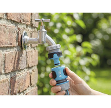 Zahradní scéna s vodovodním kohoutkem, k němuž je v ruce připojen konektor zahradní hadice for_q