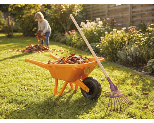 Zahradní scéna s kolečkem, hráběmi a dítětem sbírajícím listí