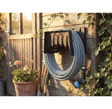 Zahradní scéna s navijákem hadice, namontovaným na dřevěné stěně s zahradní hadicí